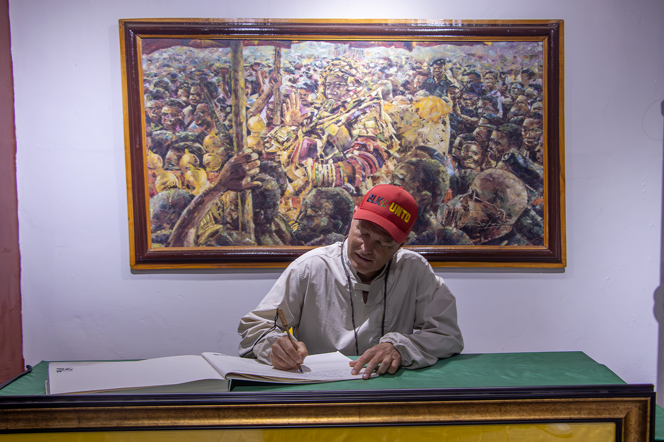 A Take Em Home traveler signing a museum guest book beneath Ghanaian art